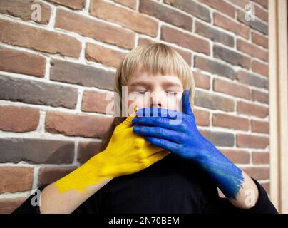 Gesicht eines Kindes mit geschlossenen Augen, bedeckt mit Händen in Farben der ukrainischen Flagge. Beenden Sie den Krieg. Angst und Machtlosigkeit. Stehen Sie auf der Seite der Ukraine. Konzept Stockfoto