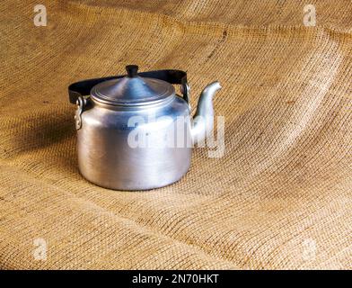 Eine alte Soldatenteekanne aus Aluminium aus dem Zweiten Weltkrieg vor dem Hintergrund von Leinenholz. Stockfoto