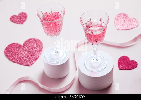 Ein Paar hält zwei rosafarbene Cocktails zum Valentinstag. Liebes- und Jubiläumsatmosphäre mit Herzen. Romantisches Konzept Stockfoto