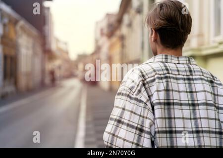 Eine Frau mit kurzen Haaren im karierten Hemd, die in der Stadt die Straße entlang läuft. Stockfoto