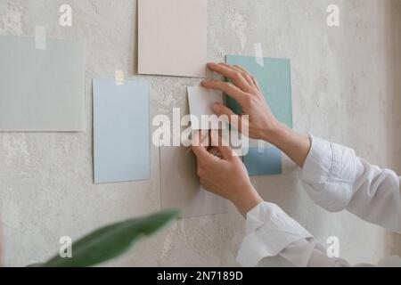 Nahaufnahme einer Frau, die Farbpapiermuster an eine Wand klebt Stockfoto
