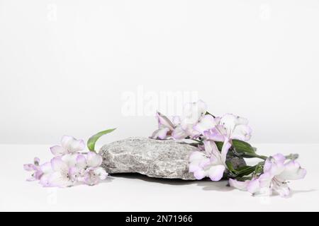 Betonsteinpodium auf weißgrauem Hintergrund mit harten Schatten und Pflanzen, Blumen. Minimale leere Präsentationsszene für kosmetische Produkte. Geometrisches Bild Stockfoto