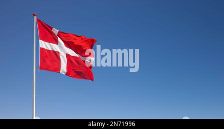 Die dänische Nationalflagge winkt im Wind gegen den blauen Himmel Stockfoto