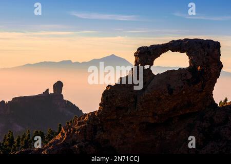 Silhouette von Roque Nublo und natürlicher Felsbogen bei Sonnenuntergang mit dem Berg Teide in der Ferne, Gran Canaria, Kanarische Inseln, Spanien Stockfoto