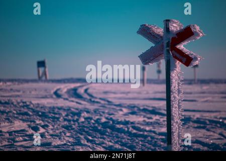 Rote Kreuzung bedeckt mit Schnee und Eis auf einem Winterpfad. Stockfoto