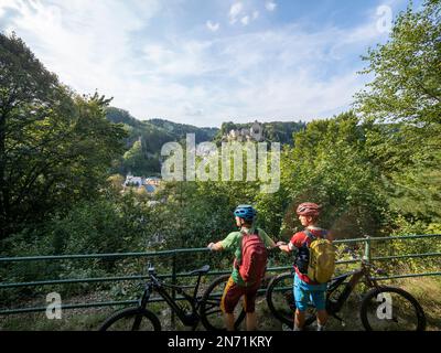 E-Mountainbiker über Larochette mit Blick auf Schloss Larochette und Schloss Fels in Larochette, Luxemburg. Die ersten Gebäude des Dorfes stammen aus dem 11. Jahrhundert und befinden sich auf einer Landzunge des luxemburgischen Sandsteins mit Blick auf das Tal des Weißen Ernz, einen Nebenfluss der Sure, ca. 150 Meter entfernt Stockfoto