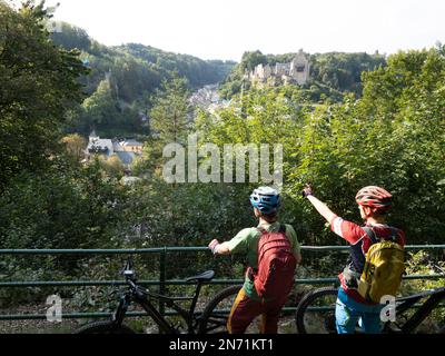 E-Mountainbiker über Larochette mit Blick auf Schloss Larochette und Schloss Fels in Larochette, Luxemburg. Die ersten Gebäude des Dorfes stammen aus dem 11. Jahrhundert und befinden sich auf einer Landzunge des luxemburgischen Sandsteins mit Blick auf das Tal des Weißen Ernz, einen Nebenfluss der Sure, ca. 150 Meter entfernt Stockfoto