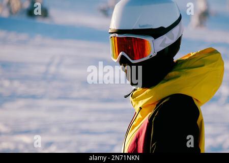 Ein junger Skifahrer in leuchtend gelber Jacke steht auf den Skiern und schaut in die Kameraobjektive. Stockfoto