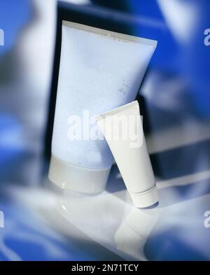 Gruppe von Kosmetikröhren und -Gläsern für Eigenmarken in reflektierenden Konzeptstudiofotos. Insgesamt ist diese Farbe Blau. Stockfoto