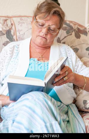 Pensionierung: Bücherwurm. Eine Seniorin sitzt, um zu lesen, sich zu entspannen und sich auf ihr Lieblingsbuch zu konzentrieren. Aus einer Reihe von zugehörigen Bildern. Stockfoto