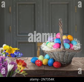 Korb aus Korb mit hell bemalten Ostereiern auf Holztisch im Innenbereich Stockfoto