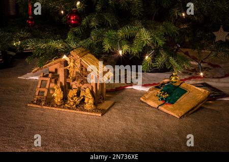 Geburtsszene mit heiliger Familie und Tieren unter einem dekorierten Weihnachtsbaum, eine Nordmanntanne mit roten und gelben Kugeln und Beleuchtung mit elektrischen Kerzen, Stockfoto