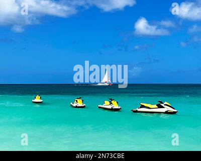 Wasserfahrzeuge, die vor der Küste von Aruba auf dem Karibischen Meer stehen. Ein Segelboot im Hintergrund. Stockfoto