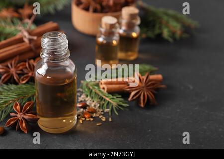 Flasche ätherisches Öl, Anis, Zimt und Tannenäste auf schwarzem Tisch Stockfoto