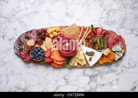 Holzteller mit verschiedenen leckeren Snacks auf weißem Marmortisch, Blick von oben Stockfoto