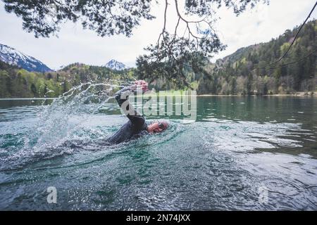 Professioneller Triathlet Schwimmen, Training in einem klaren Bergsee in Allgäu, Alatsee, Bayern, Deutschland Stockfoto