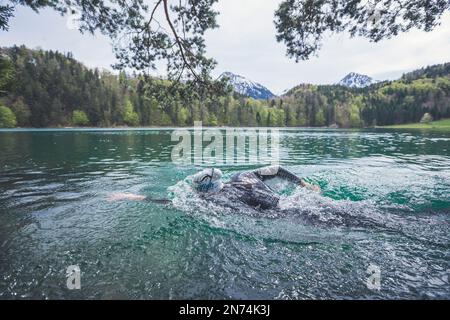Professioneller Triathlet Schwimmen, Training in einem klaren Bergsee in Allgäu, Alatsee, Bayern, Deutschland Stockfoto