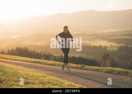 Profitriathleten laufen, Morgenatmosphäre, Sonnenaufgang, Auerberg, Allgäu, Bayern, Deutschland Stockfoto