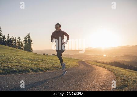 Profitriathleten laufen, Morgenatmosphäre, Sonnenaufgang, Auerberg, Allgäu, Bayern, Deutschland Stockfoto