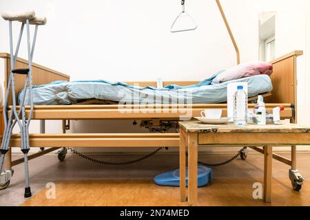 Seitenansicht von Homecare verstellbaren elektrischen Krankenhausbett, Krücken und Tisch mit Medizin zu Hause Stockfoto