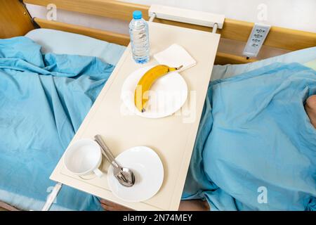 Über dem Blick auf Geschirr und Banane auf dem Tisch auf dem elektrischen Krankenhausbett mit Patient zu Hause Stockfoto