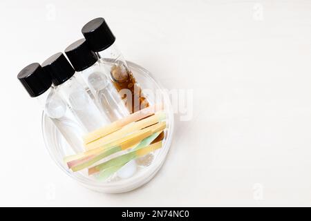 Ansicht mehrerer Reagenzgläser mit Flüssigkeiten und Lösungen und Lackmuspapier in Glasschale auf einem beleuchteten Schreibtisch mit Kopierraum Stockfoto