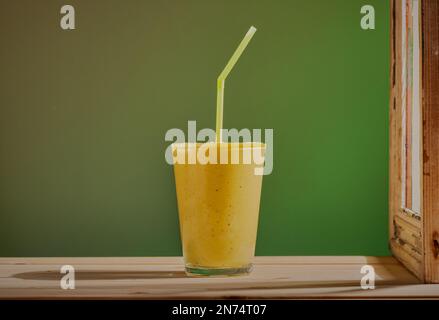 Lebhaftes Smoothie-Getränk mit Strohhalm, das auf einem Holztisch vor einem Fenster ruht und ein Licht auf das Getränk strahlt. Stockfoto