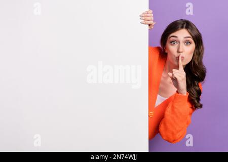 Foto einer jungen, flippigen Promoterin, die ein orangefarbenes Hemd trägt, das hinter einem riesigen Werbeschild mit lilafarbenem Hintergrund eine stumme Fahne zeigt Stockfoto