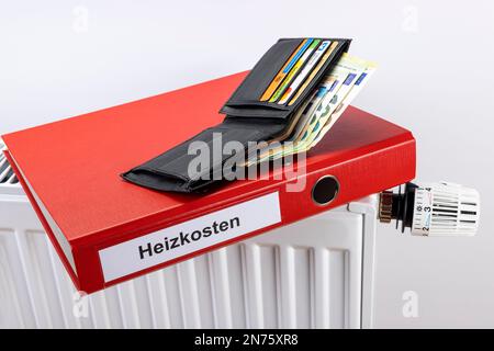 Schwarze Tasche, roter Aktenordner mit Energiekosten auf dem Etikett, Heizkörperthermostat, Einstellstufe 4 ca. Stockfoto