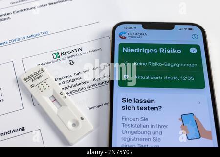 Zertifizierung, Nachweis, Ergebnis, SARS-CoV-2-Schnelltest, SARS-CoV-2-Antigen-Schnelltestkassette mit negativem Testergebnis, iPhone Corona Warnung App geöffnet, geringes Risiko grün, Detail, weißer Hintergrund, Stockfoto