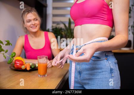 Frau misst ihre Taille mit Maßband in Gesellschaft eines Freundes Stockfoto