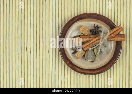 Muskatnuss, Zimt, Koriander, Anis und Rohrzucker auf einem Teller mit Strohhintergrund. Gewürze für die Zubereitung von heißen Getränken. Draufsicht. Stockfoto