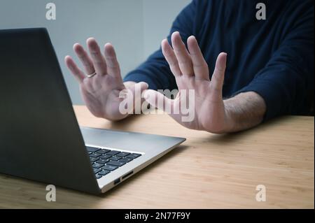 Hände in defensiver Geste gegen einen Laptop, um weitere Arbeit an einem gehackten System oder andere Gefahren und Vergehen zu vermeiden, Online-Risiken im Geschäft und Stockfoto