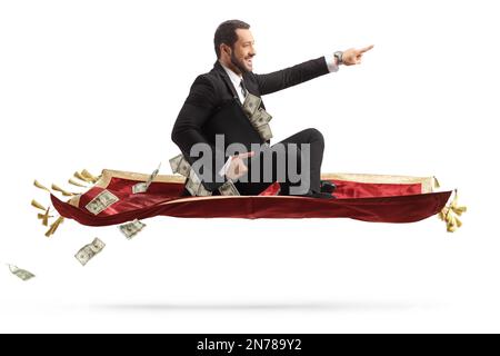 Ein Geschäftsmann, der eine Aktentasche mit Geld in der Hand hält, auf einem fliegenden Teppich sitzt und isoliert auf weißen Hintergrund zeigt Stockfoto