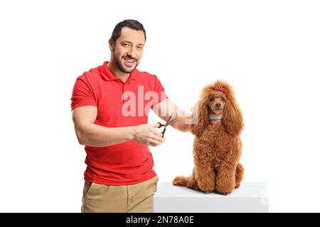 Ein Mann, der einen roten Pudelhund mit einer Schere pflegt und lächelt, isoliert auf weißem Hintergrund Stockfoto