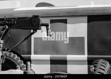 Hinter einem Maschinengewehr, das während einer Nachstellung im American Heritage Museum auf einem Jeep montiert ist, ist ein LKW mit einem großen Roten Kreuz zu sehen. Die Stockfoto