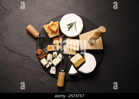 Käseplatte mit Spezialmessern und Gabel auf schwarzem Tisch, flach liegend Stockfoto