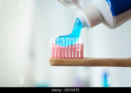 Auftragen von Zahnpasta auf die Bürste vor unscharfem Hintergrund, Nahaufnahme Stockfoto