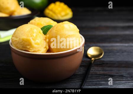 Leckeres Mangoeis in der Schüssel auf einem schwarzen Holztisch. Platz für Text Stockfoto