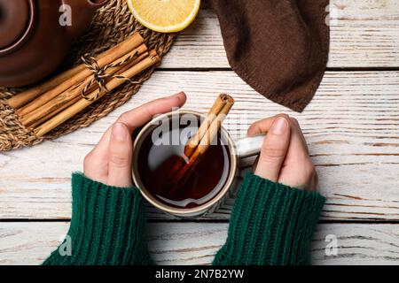 Eine Frau, die eine Tasse köstlichen heißen Tee mit Zimt auf einem weißen Holztisch hielt, Draufsicht Stockfoto