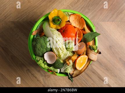 Abfalleimer mit organischem Abfall zur Kompostierung auf Holzhintergrund, Draufsicht Stockfoto