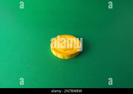 Papierausschnittsmodell eines gelben 3D-Bitcoin-Tokens auf minimalistischem Hintergrund, Krypto-Blockchain papercraft-Kunst auf flachem grünen Hintergrund Stockfoto