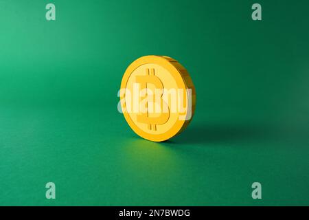 Papierausschnittsmodell eines gelben 3D-Bitcoin-Tokens auf minimalistischem Hintergrund, Krypto-Blockchain papercraft-Kunst auf flachem grünen Hintergrund Stockfoto