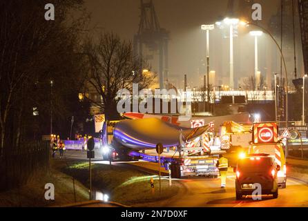 Hamburg, Deutschland. 10. Februar 2023. Ein Schwerlasttransport mit Rotorblättern für eine neue Windturbine ist auf dem Weg von der Autobahnausfahrt Waltershof im Hamburger Hafen zur Kläranlage Dradenau. Drei schwere Lkw brachten am Samstagabend große Teile einer neuen Windturbine nach Hamburg-Waltershof. Nach Angaben des Betreibers der Kläranlage Hamburg Wasser wird die neue Windturbine eine Leistung von 3,6 Megawatt haben und jährlich 9.000 Megawatt-Stunden Strom liefern. Kredit: Christian Charisius/dpa/Alamy Live News Stockfoto