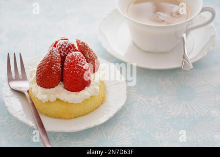 Frische süße Erdbeeren mit Schlagsahne auf einer Dessertttasse mit gelbem Schwamm und einer Tasse Tee in horizontaler Form. Stockfoto