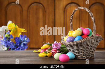 Korb aus Korb mit bunt lackierten Ostereiern auf Holztisch im Innenbereich, Platz für Text Stockfoto