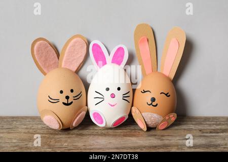 Eier als süße Häschen auf einem Holztisch vor hellgrauem Hintergrund. Osterfeier Stockfoto