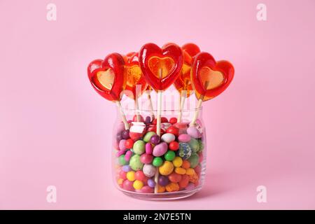 Glasbehälter mit verschiedenen Süßigkeiten auf pinkfarbenem Hintergrund Stockfoto