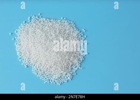 Ammoniumnitrat-Pellets auf hellblauem Hintergrund, flach liegend mit Platz für Text. Mineraldünger Stockfoto