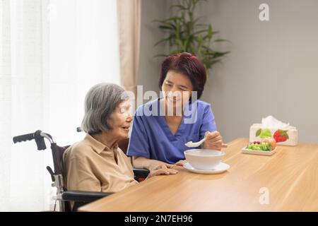 Pflegekraft füttert ältere asiatische Frau mit Suppe. Stockfoto